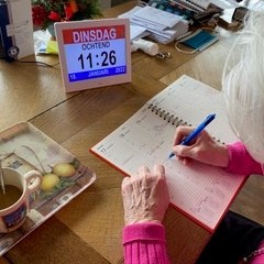 Digitale dagkalender naast een agenda waarin iemand schrijft
